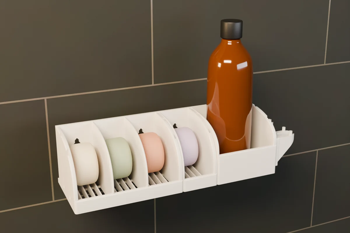 A white set on a dark tiled wall: the 3-Box Soap Holder with a 1-Box Add-On, a Bottle Holder with a bottle, and a Razor Holder.